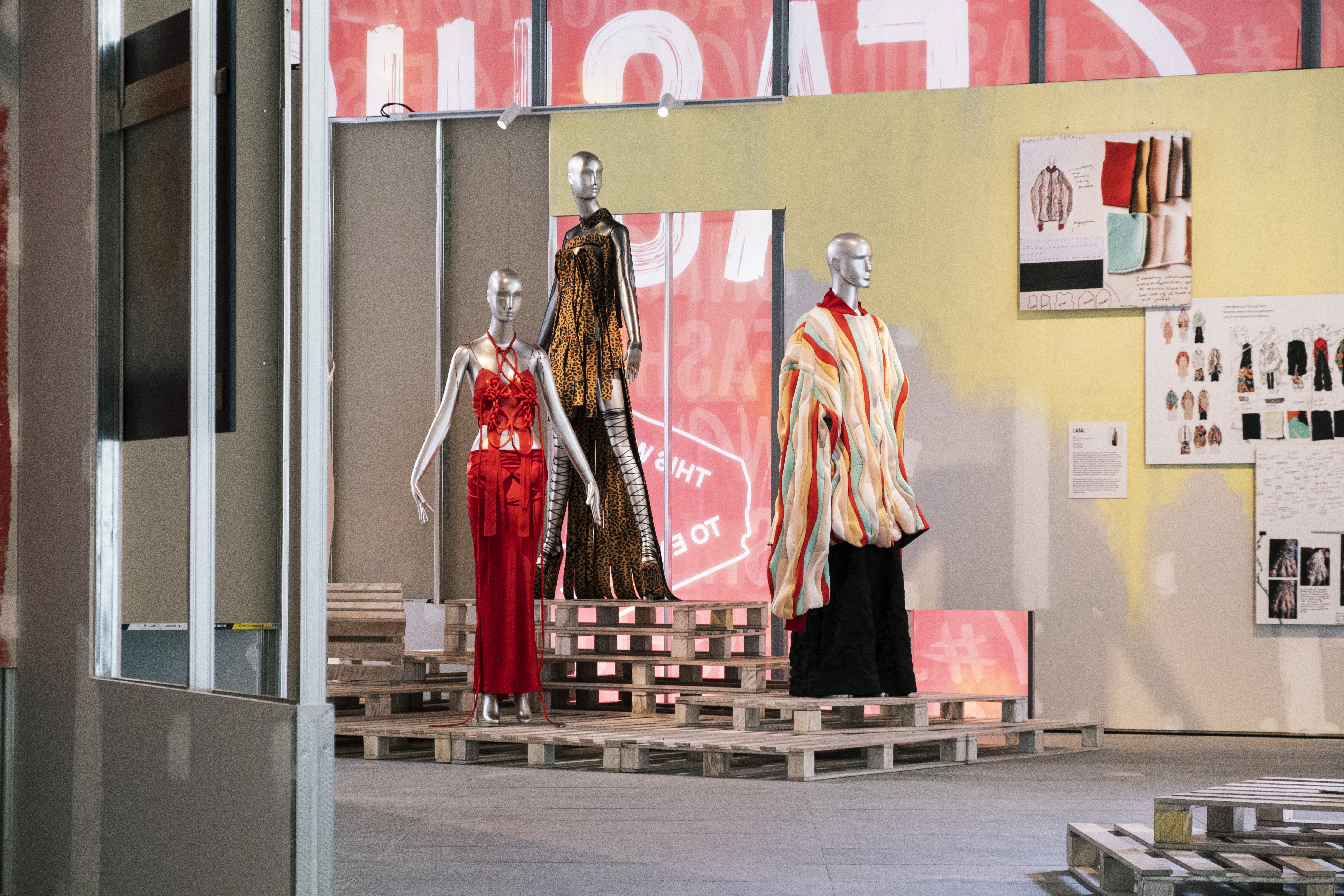 Three mannequins wearing designer clothes in a gallery standing on wooden platforms