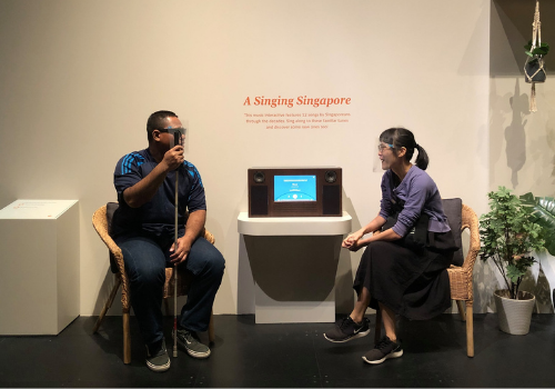 Actors Hadi and Shan Shan sitting and interacting by the exhibit "A Singing Singapore".